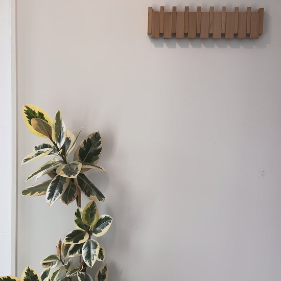 A beech Piano Hook rack sits flat against the wall, then a coat is hung on it, pushing the hooks down.