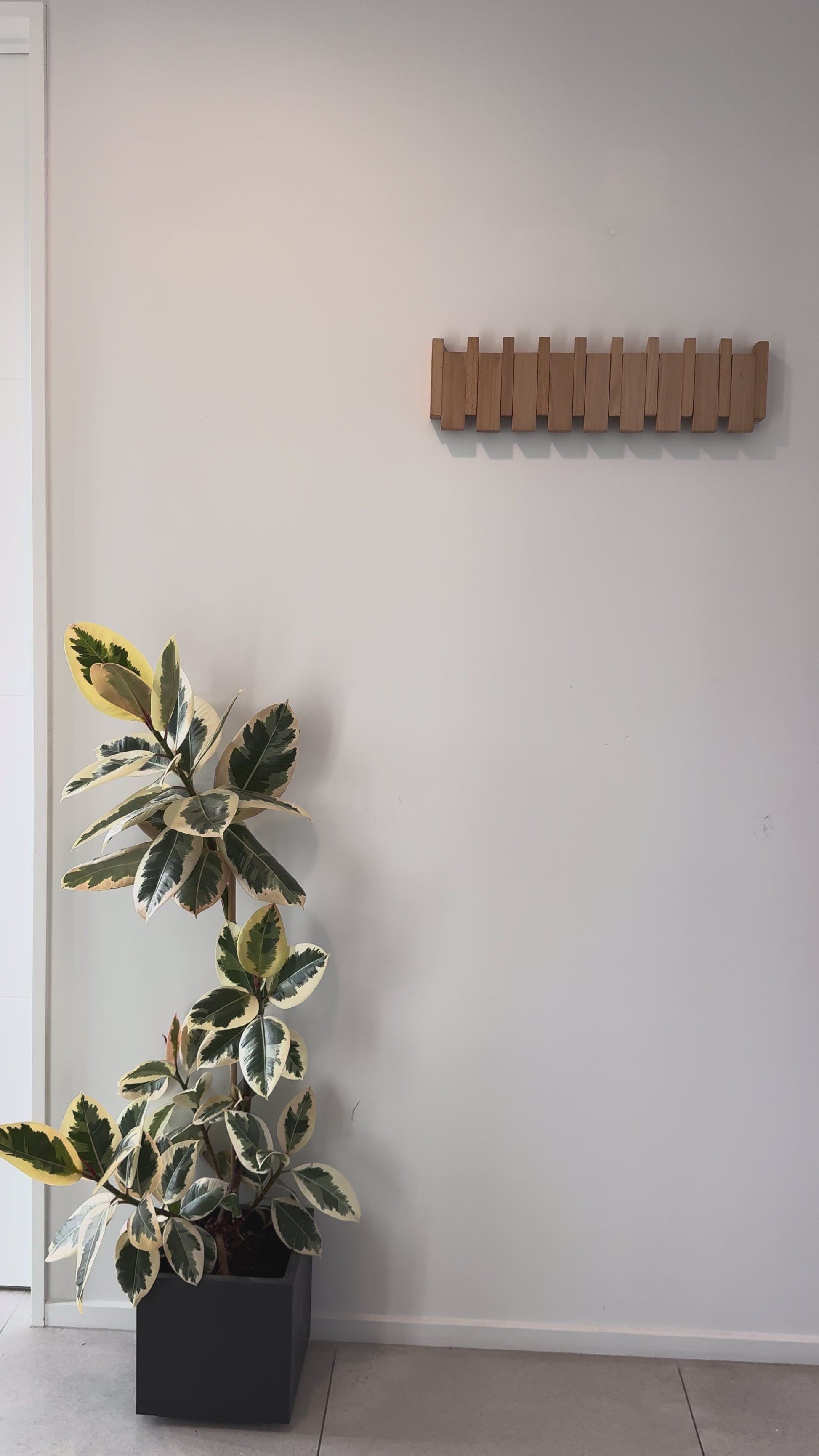 A beech Piano Hook rack sits flat against the wall, then a coat is hung on it, pushing the hooks down.